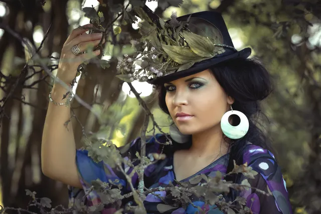 The untreated color portrait of a person in a black hat among leaves and trees.