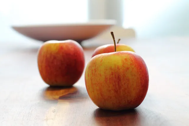 Original still life of red apples on a wooden table against a bright background.